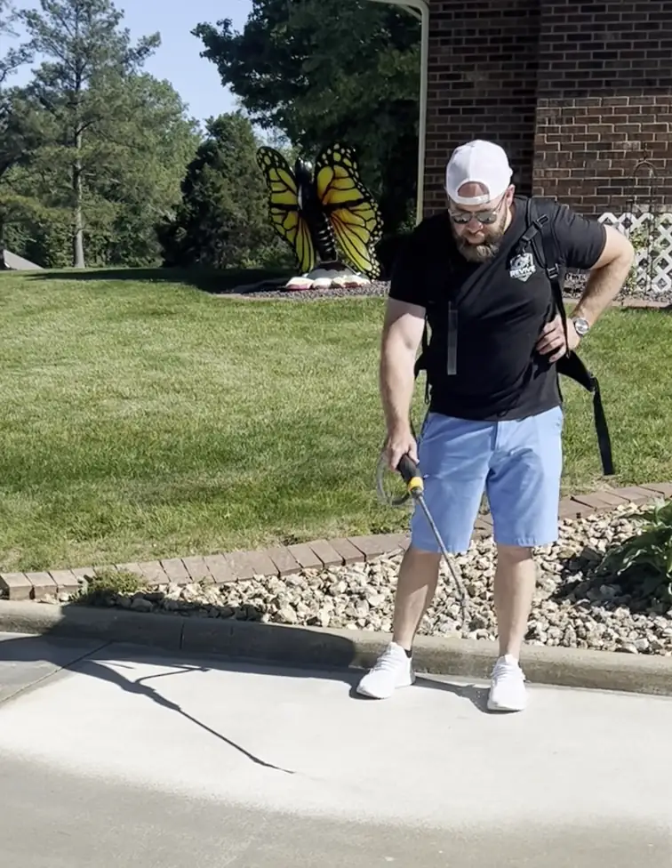 Crew member applying a protection treatment to a sidewalk with a backpack sprayer