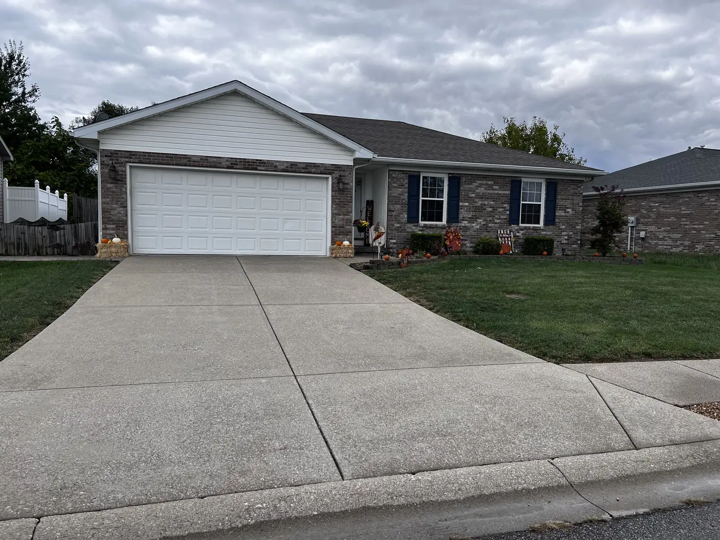 Clean concrete driveway in front of a brick ranch home with a white garage door