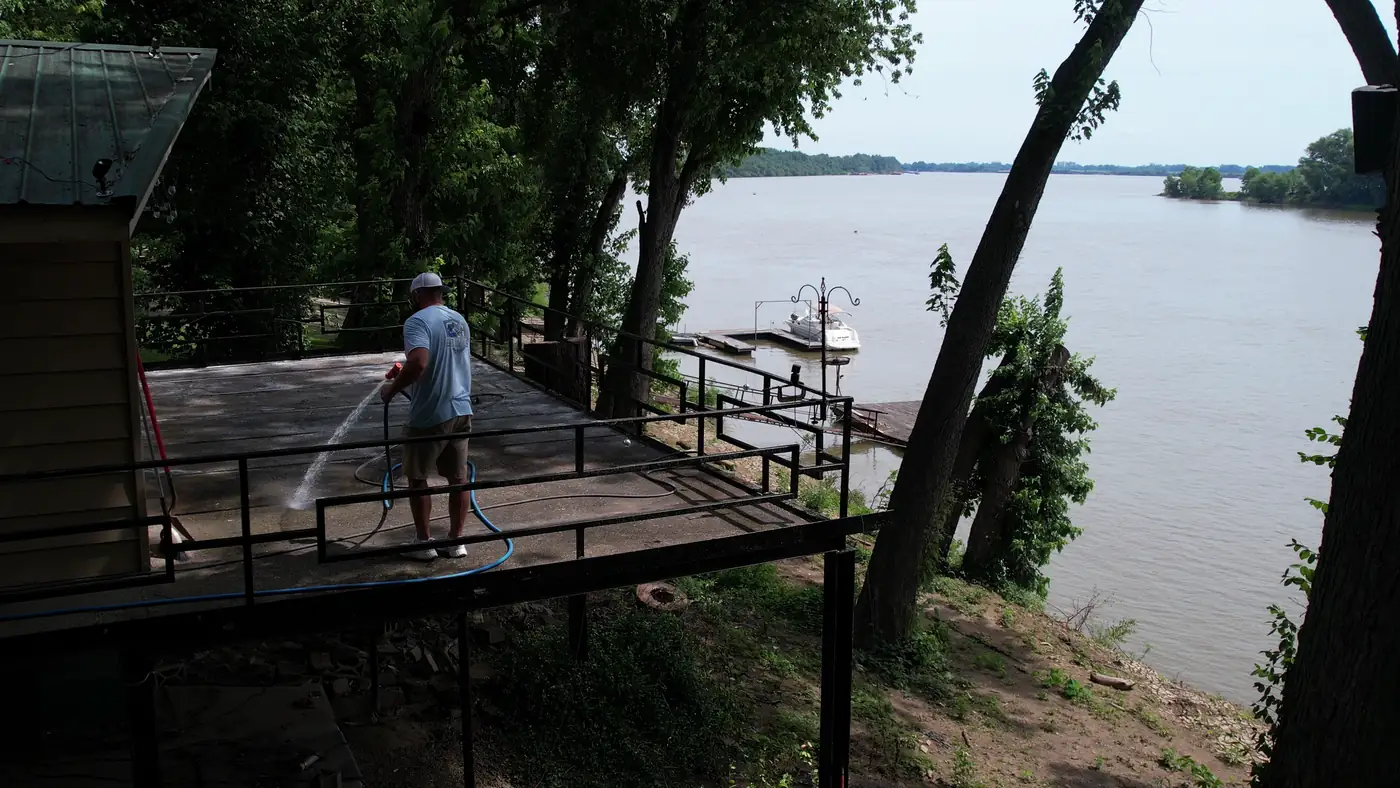 Crew member rinsing a riverfront patio with boats on the river below