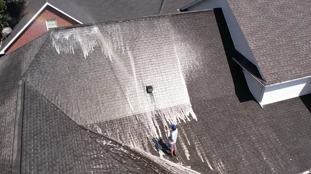 Drone view of a crew member soft washing a shingle roof, white cleaning foam running down the slope