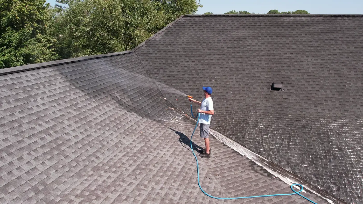 Crew member on a roof valley rinsing shingles with a low-pressure hose