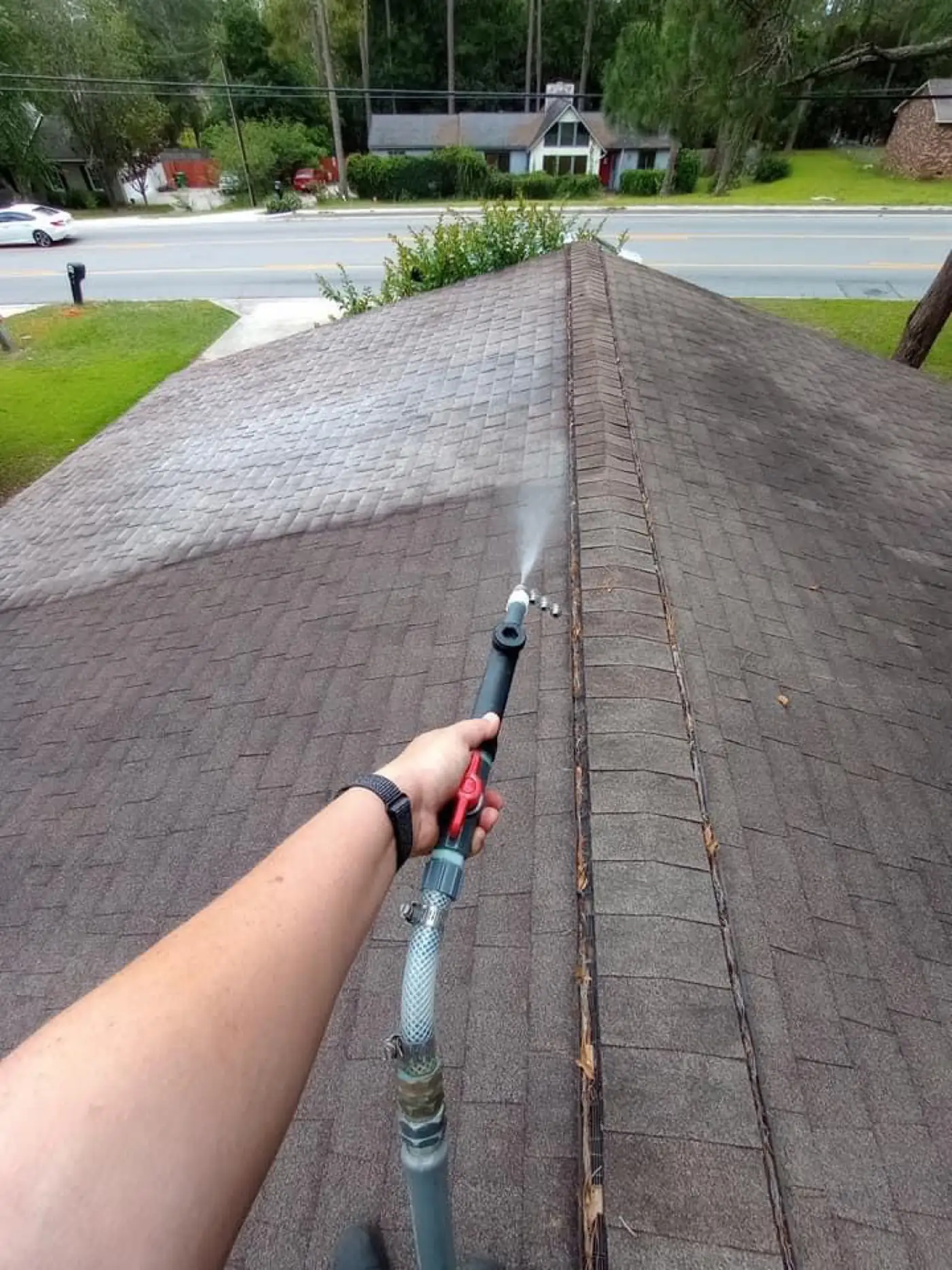 Hand holding a spray wand over a streaked shingle roof ridge
