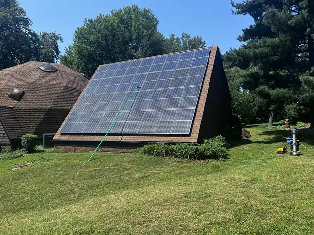 Crew member cleaning a large solar array with a water-fed pole brush