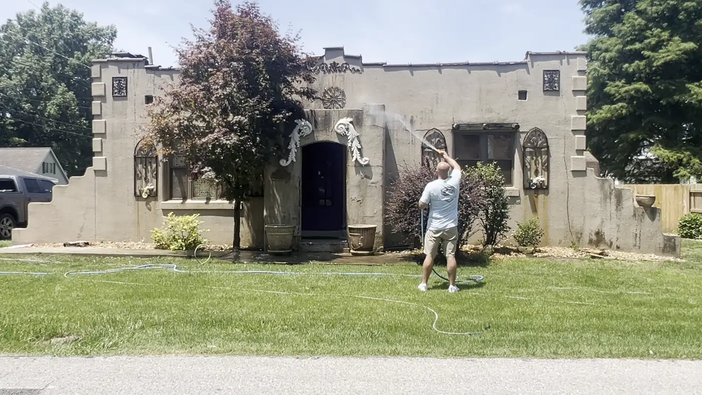 Crew member washing the front of a stucco home with arched windows